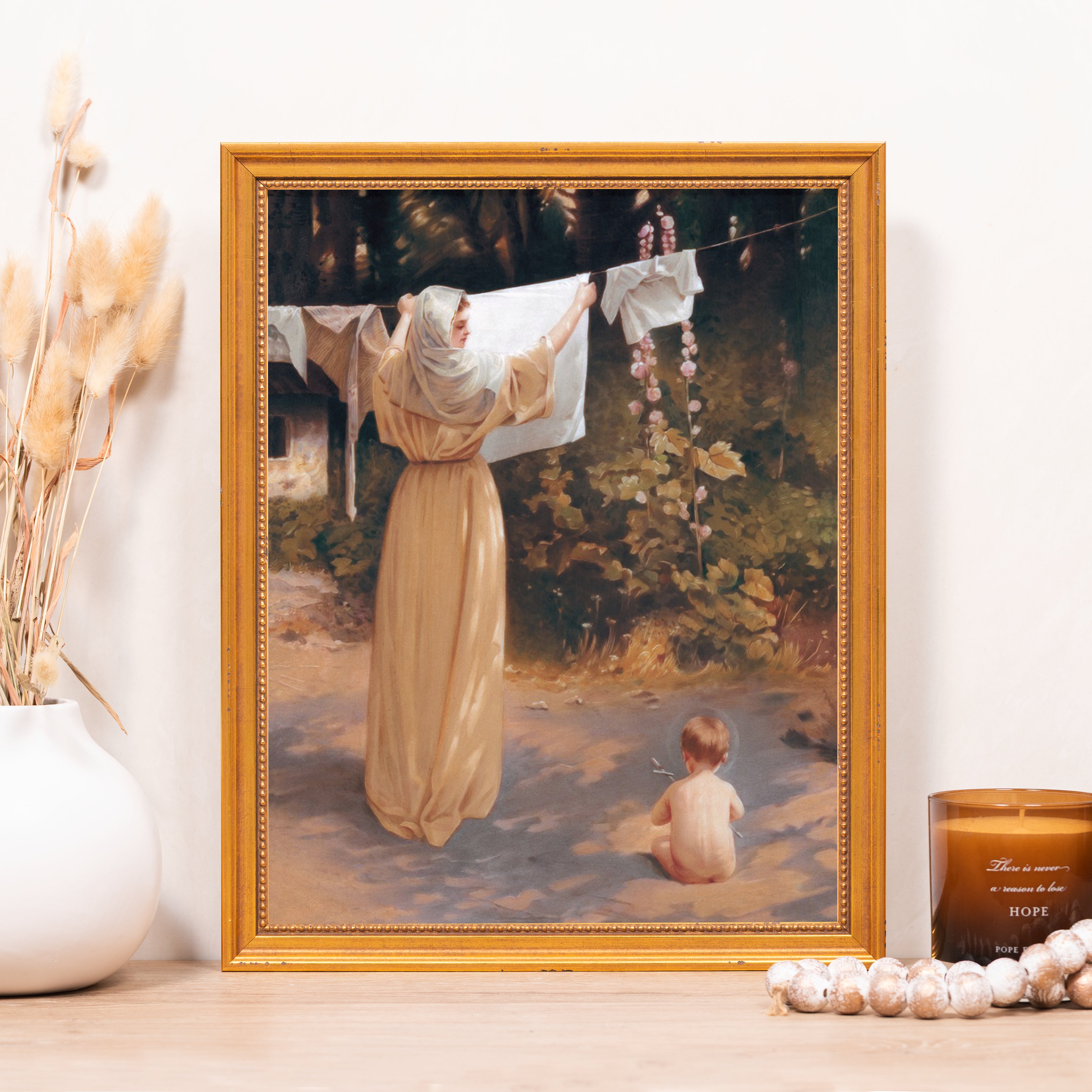 Framed painting of woman hanging laundry with a child in a golden frame.