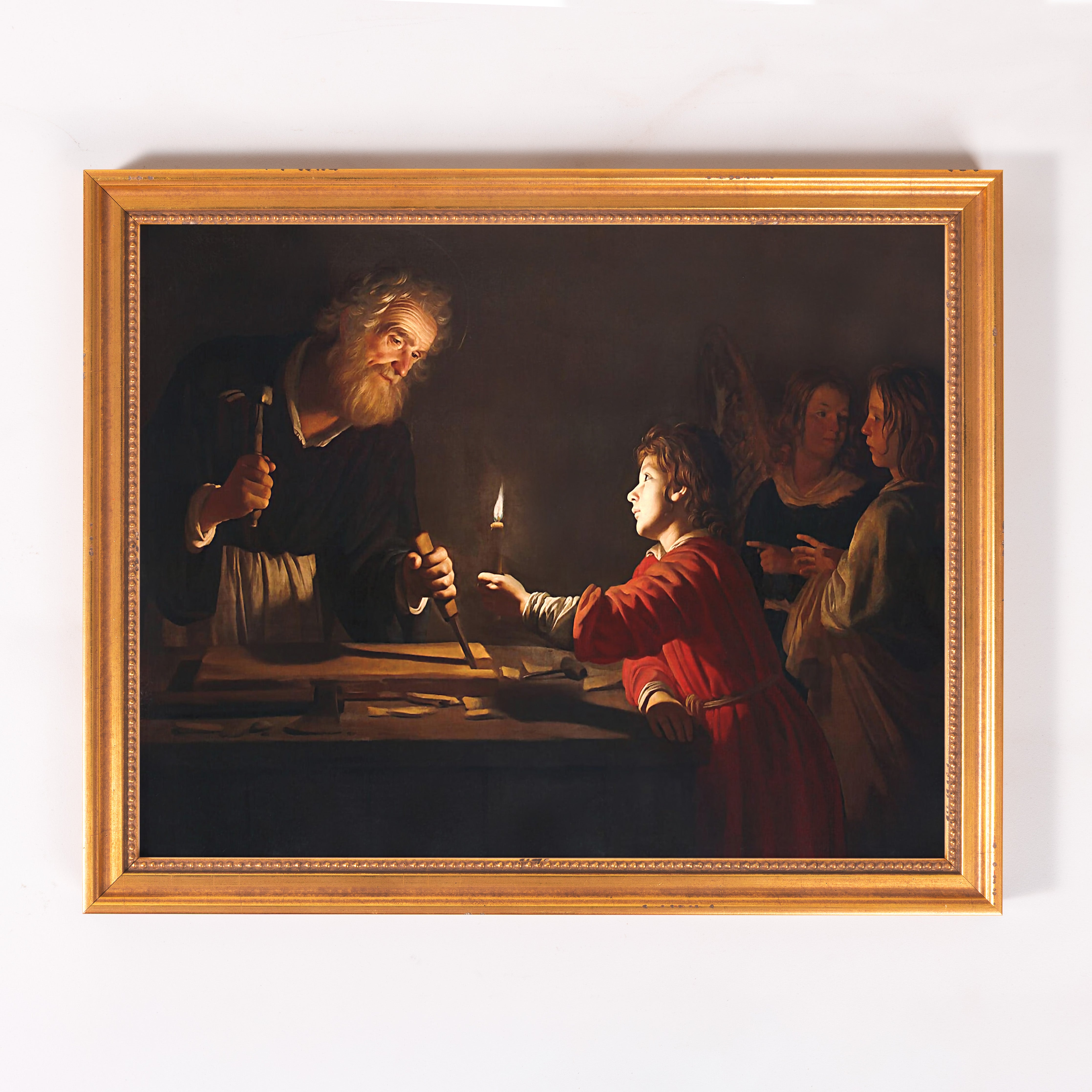 Framed oil painting of Jesus working in a carpentry shop with Joseph, lit by candlelight.
