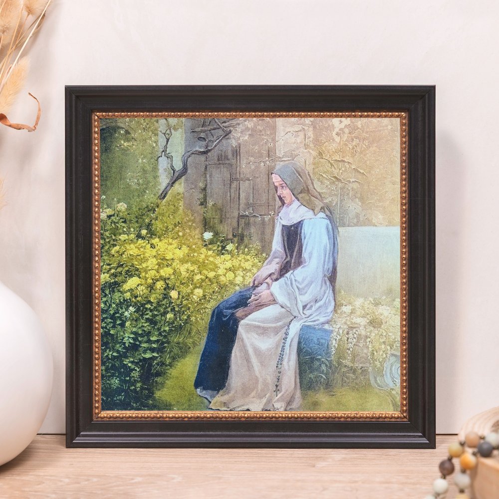 Framed print of a nun in a garden, presented in a dark wooden frame with a beaded gold border.
