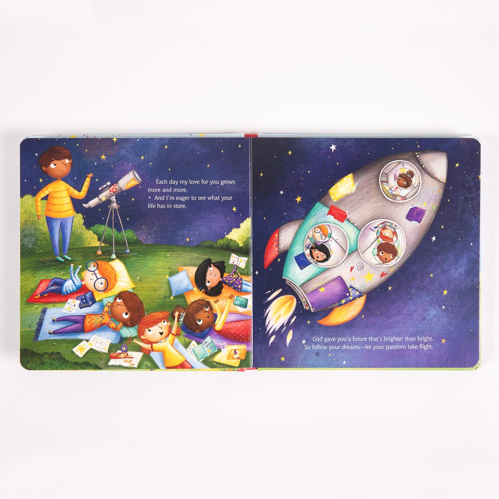 Opened children's book shows colorful illustrations of children in a grassy field and in a space rocket.