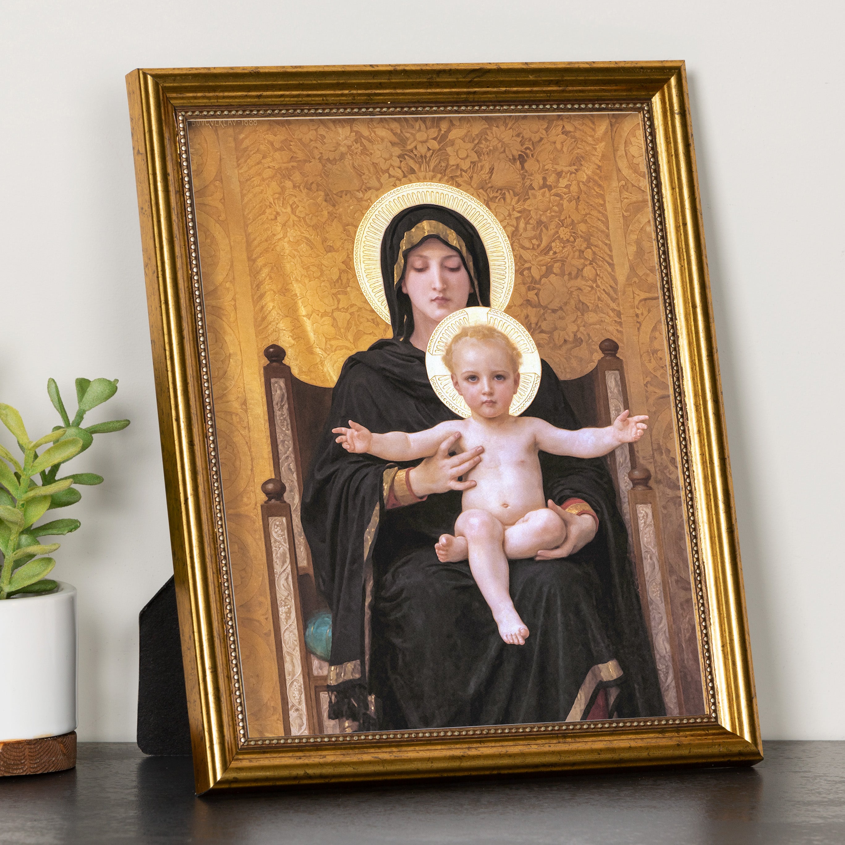 Framed Mary and Jesus painting with a gold frame, halos, and dark gowns; standing on a table.