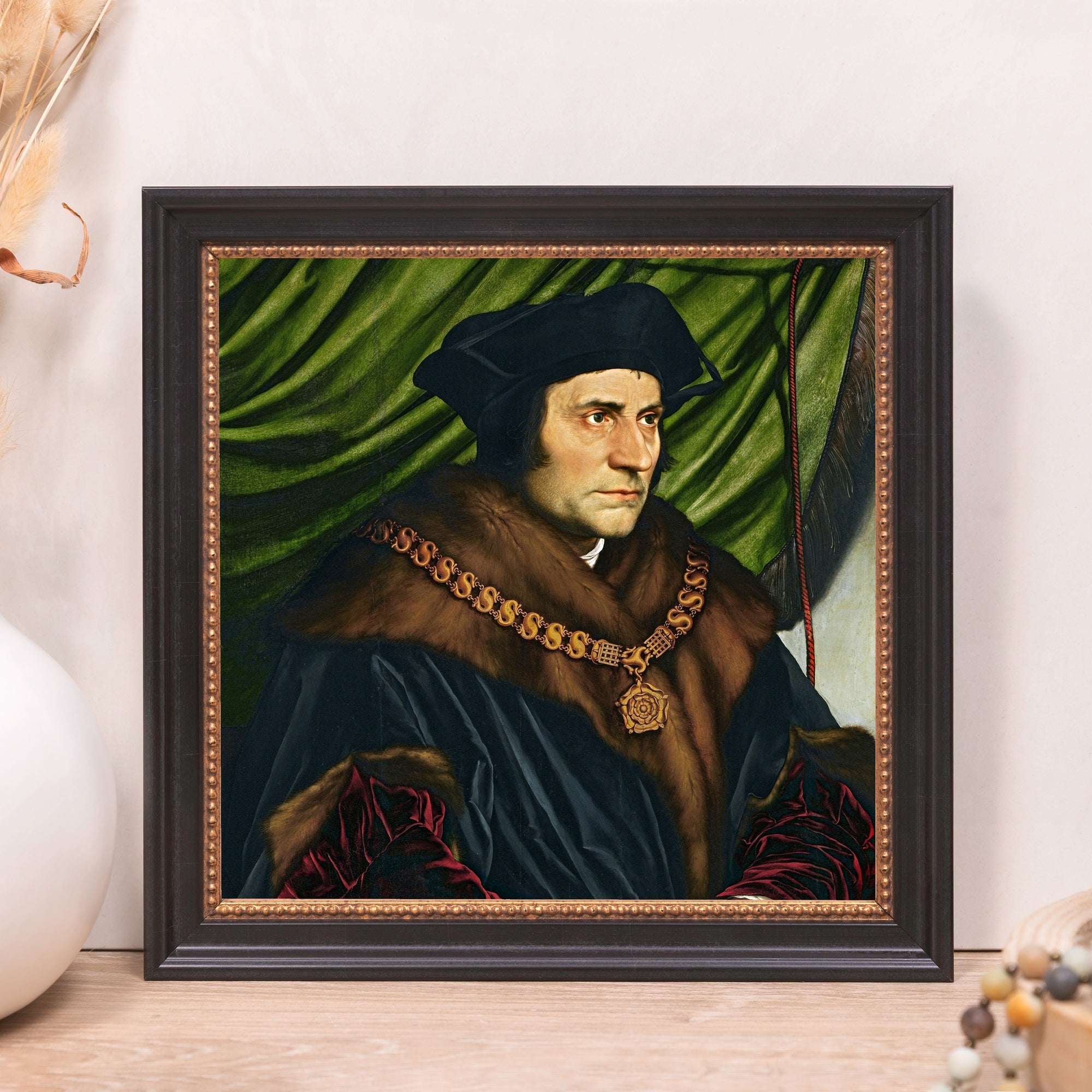 Framed portrait of a man with a fur collar and gold chain against green fabric background.