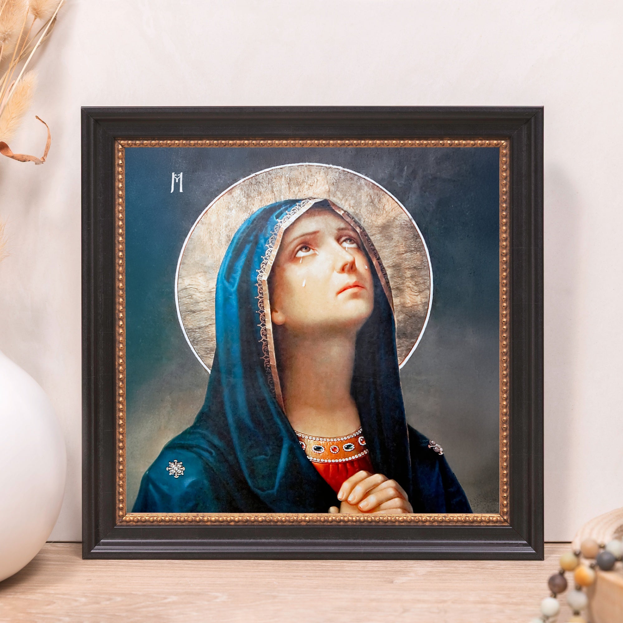 Framed Art Print of Mary with a blue veil, tears, and halo, in a black frame with gold trim.