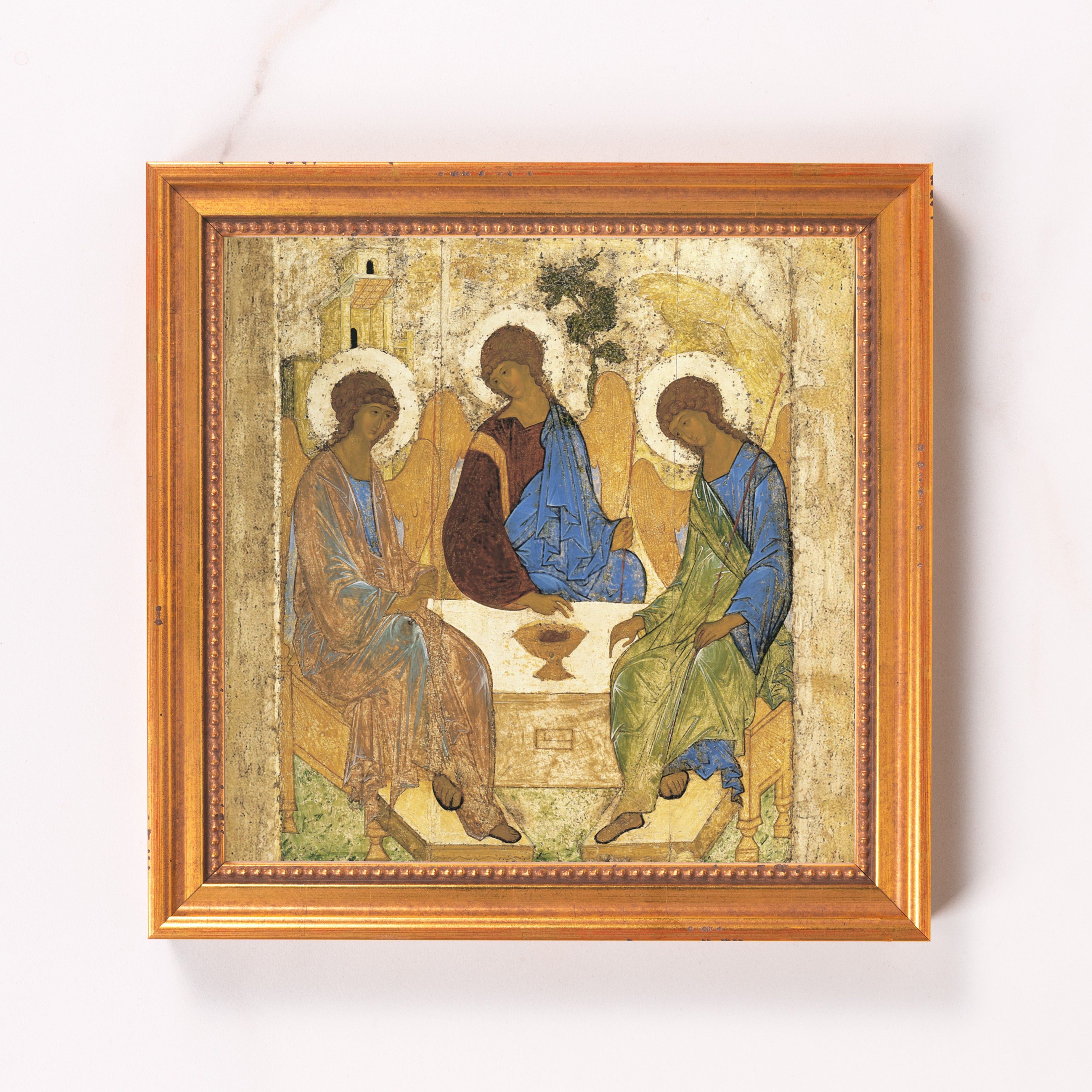 Framed painting depicts three figures with halos in blue and brown robes around a table.