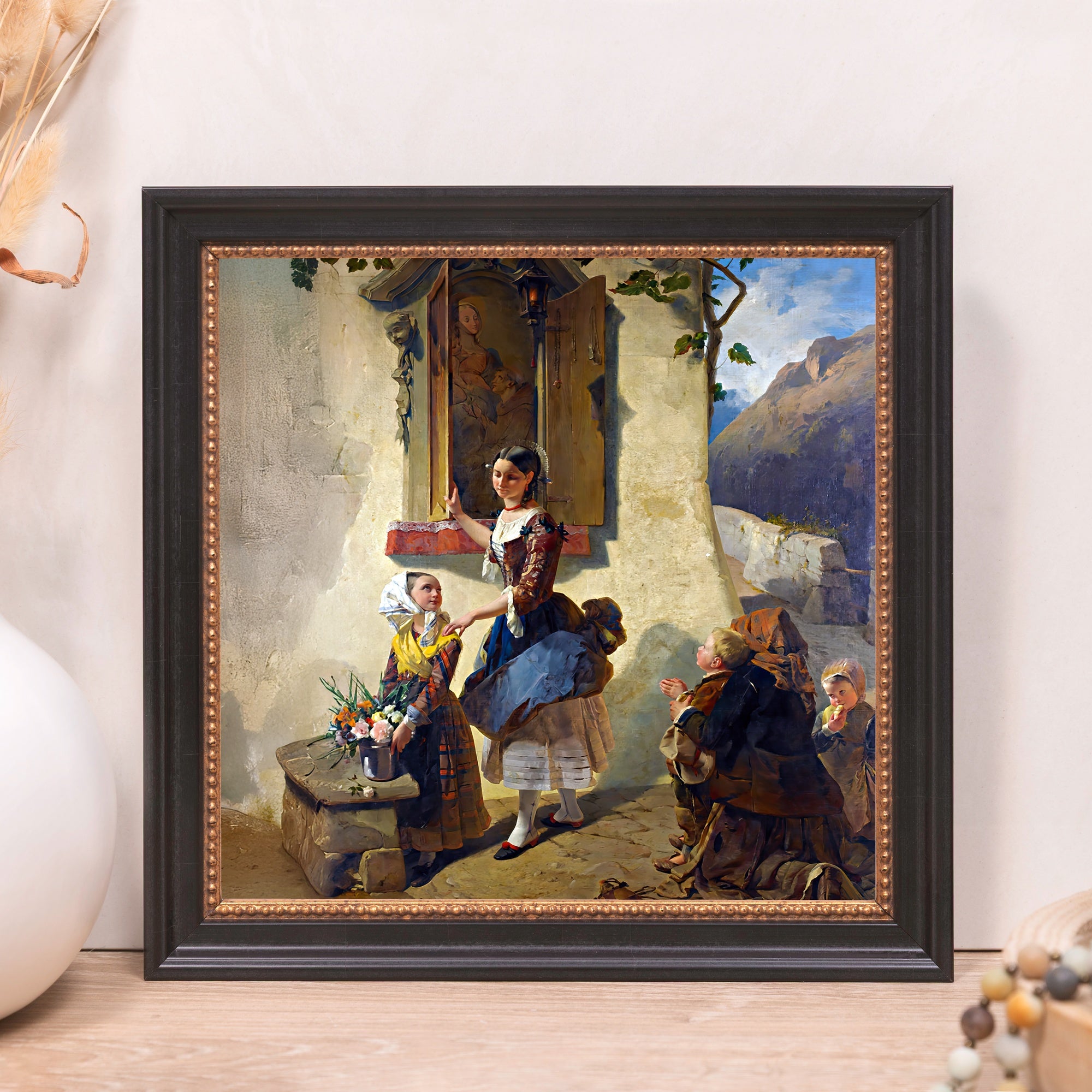 Framed art print. A dark brown frame holds a painting of people outside of a building with mountains in the background.