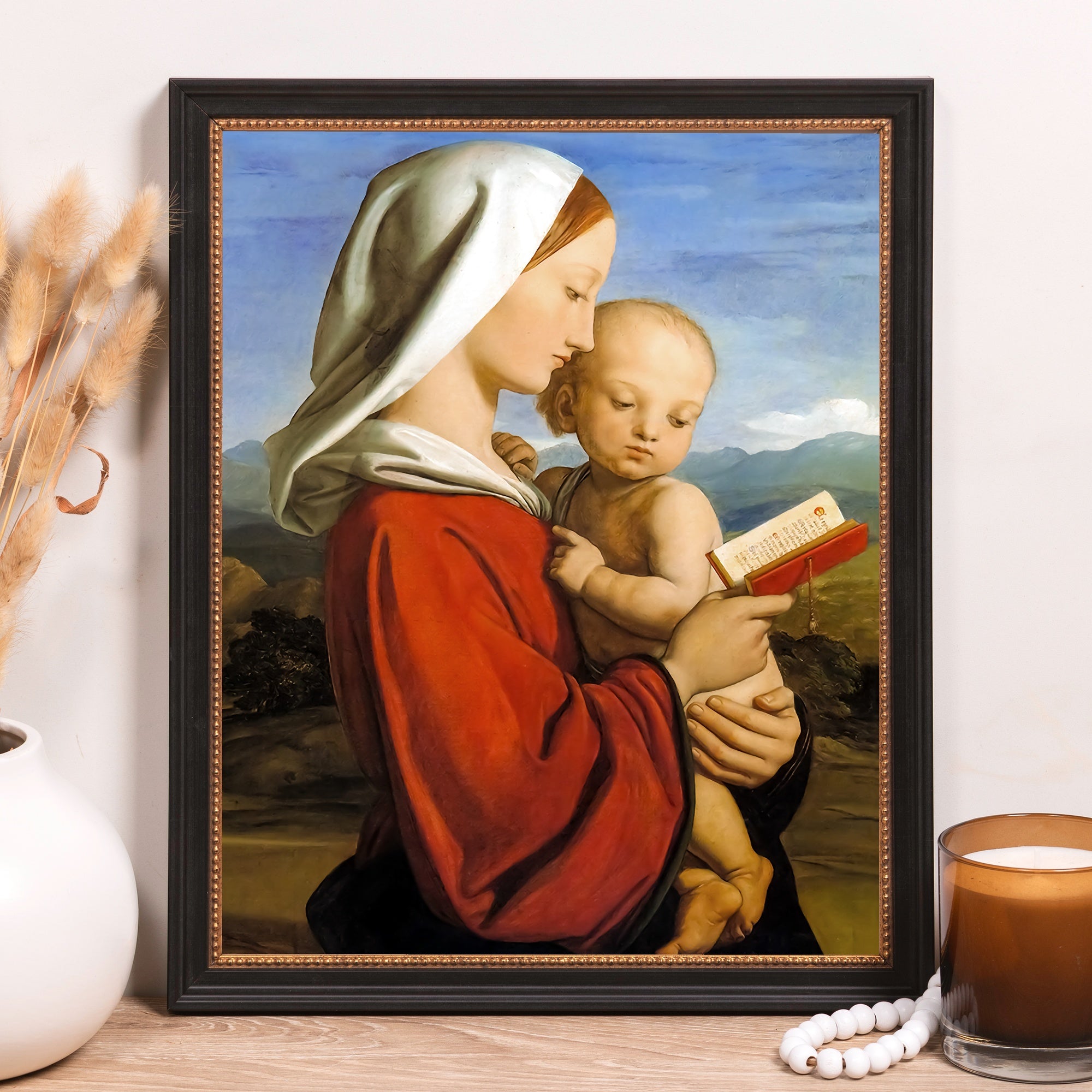 Framed Renaissance-style painting of Mary holding baby Jesus reading a book; black frame.