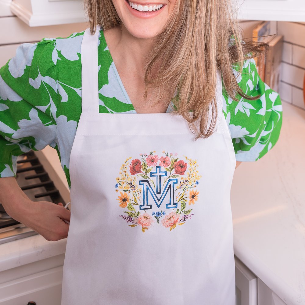 Woman Wearing a white apron with a floral design, and the letter M with a cross in the middle.
