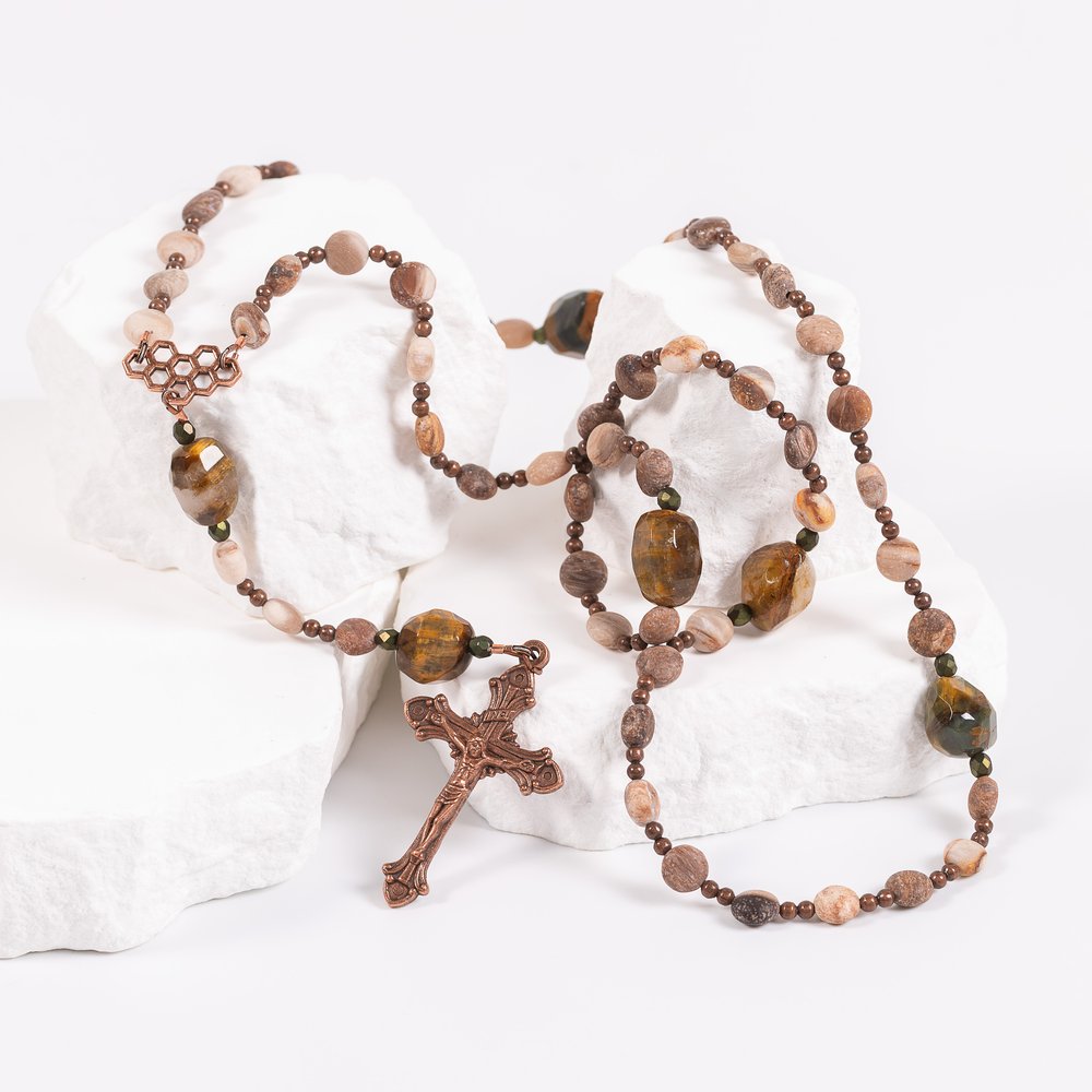 Rosary featuring wood-like beads with a copper crucifix on white rocks.