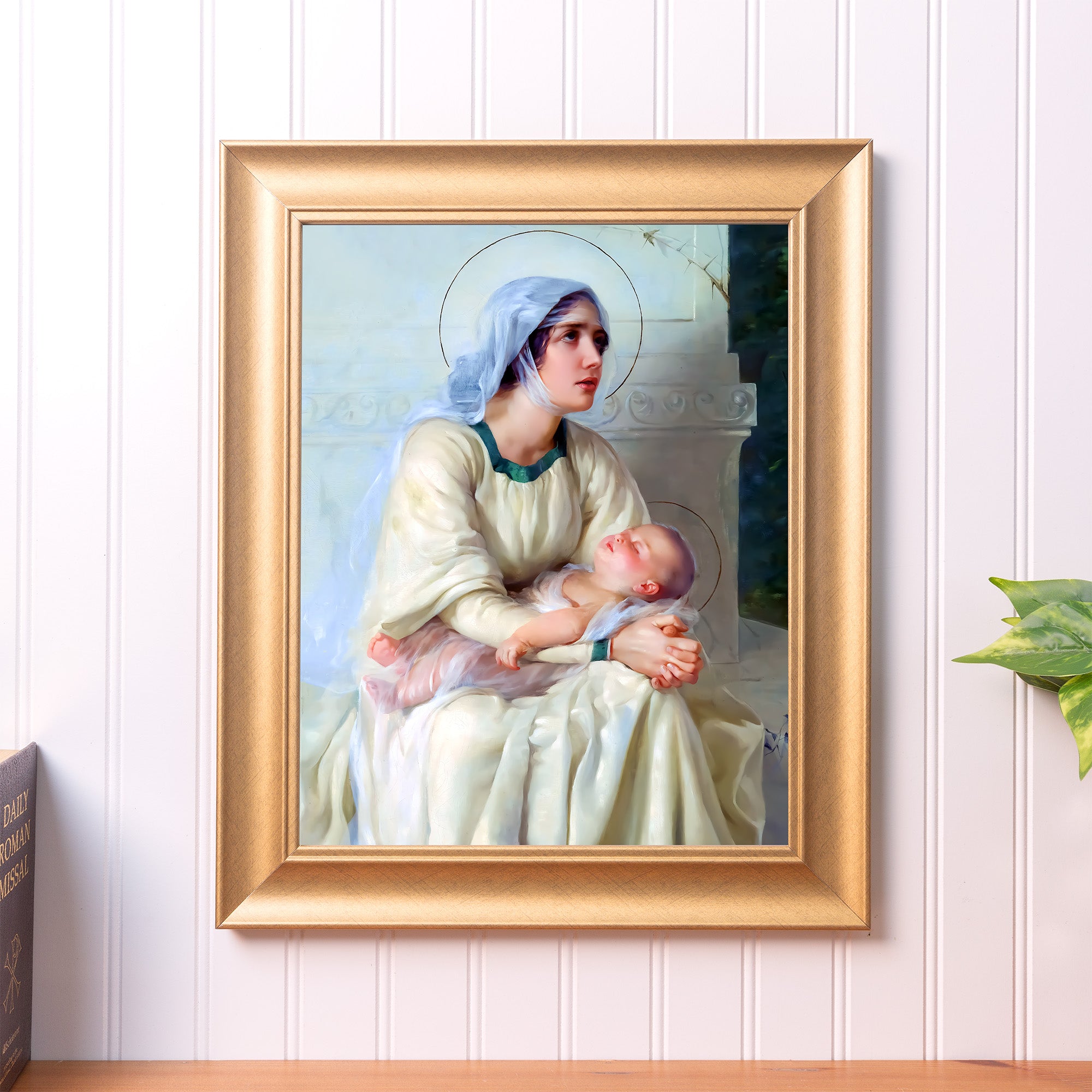 Framed religious print, Virgin Mary with baby Jesus, in a gold frame, hanging on a white wall.