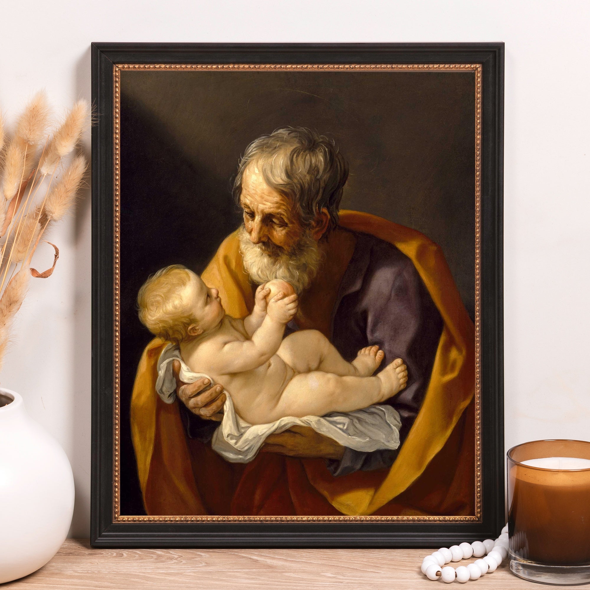 Framed oil painting depicting an old man holding a baby in his arms with yellow and purple robes.