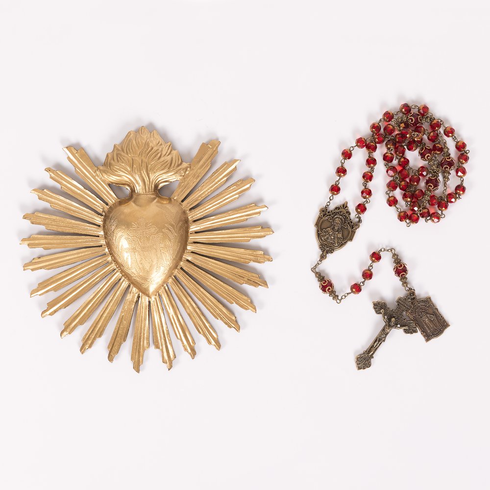 Religious items: A golden Sacred Heart wall hanging and a beaded red rosary with crucifix.