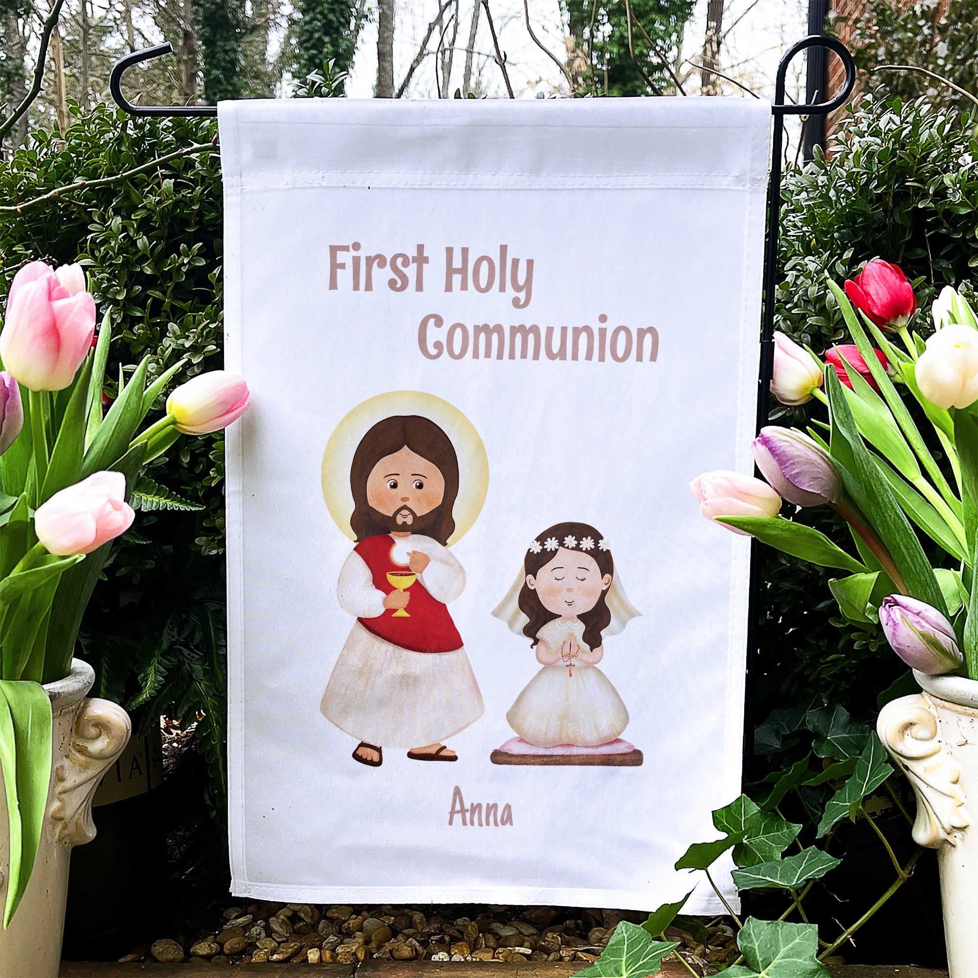 White garden flag reads "First Holy Communion" with cartoon drawings of Jesus and a child wearing a veil.