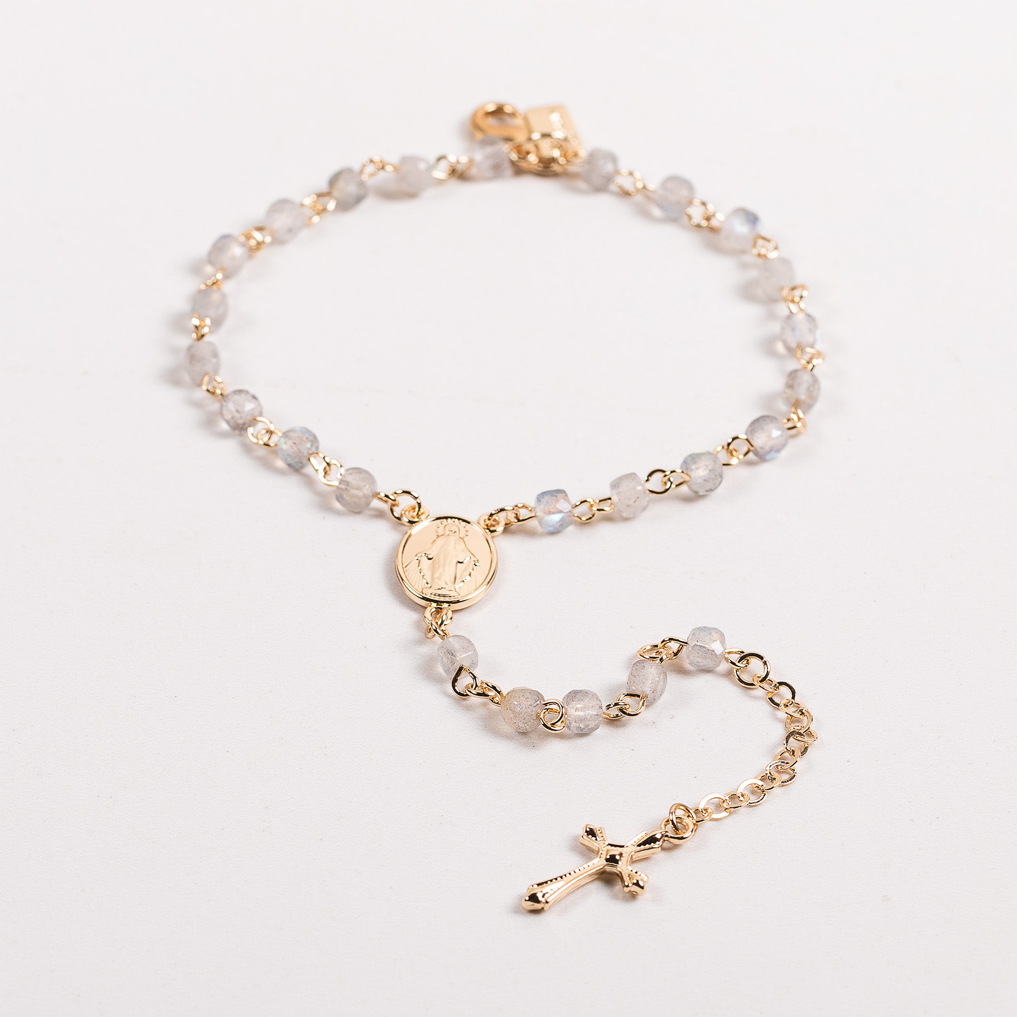 Gold rosary bracelet with gray gemstone beads and cross.