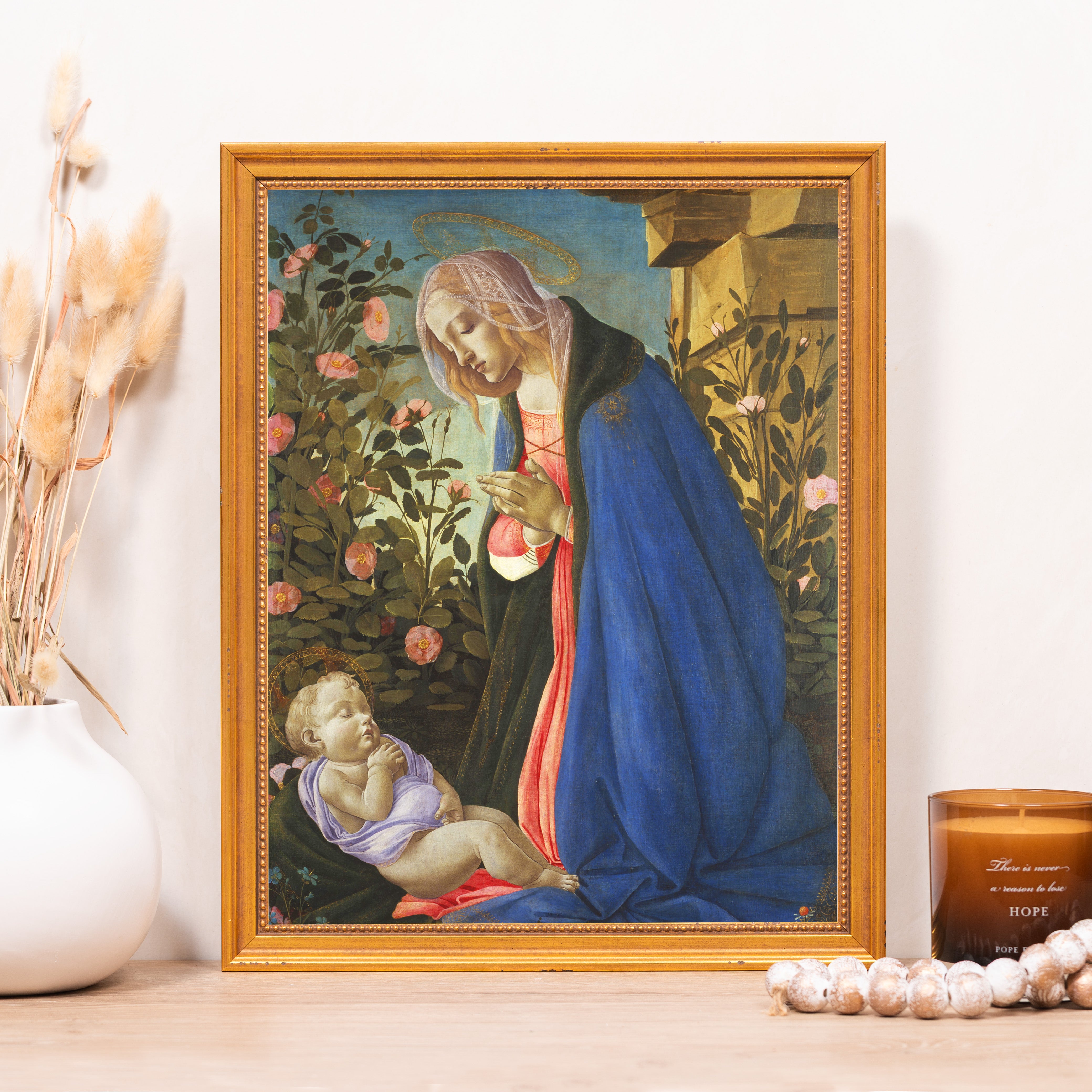 Framed art print of Mary and baby Jesus in Renaissance style with a blue gown and halo on wood table.