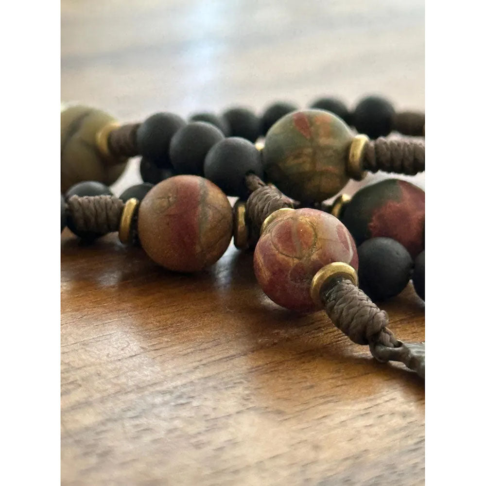 Close-up of a beaded necklace with matte black, brown, red and green beads and gold accents on brown cord.