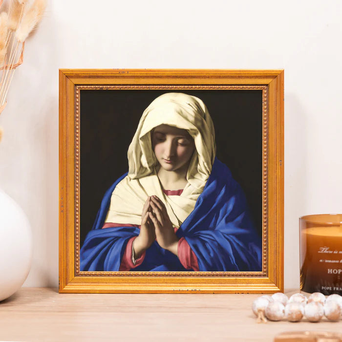 Framed artwork of the Virgin Mary praying on a tabletop.