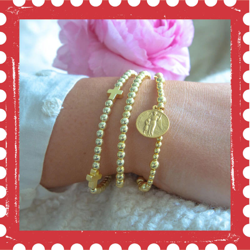 Gold bracelets on a wrist with a pink flower in the background