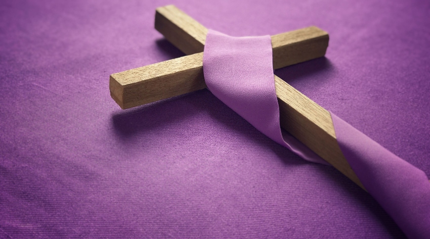 Wooden Cross on Lenten Violet Cloth - Photo Credit goodhousekeeping.org